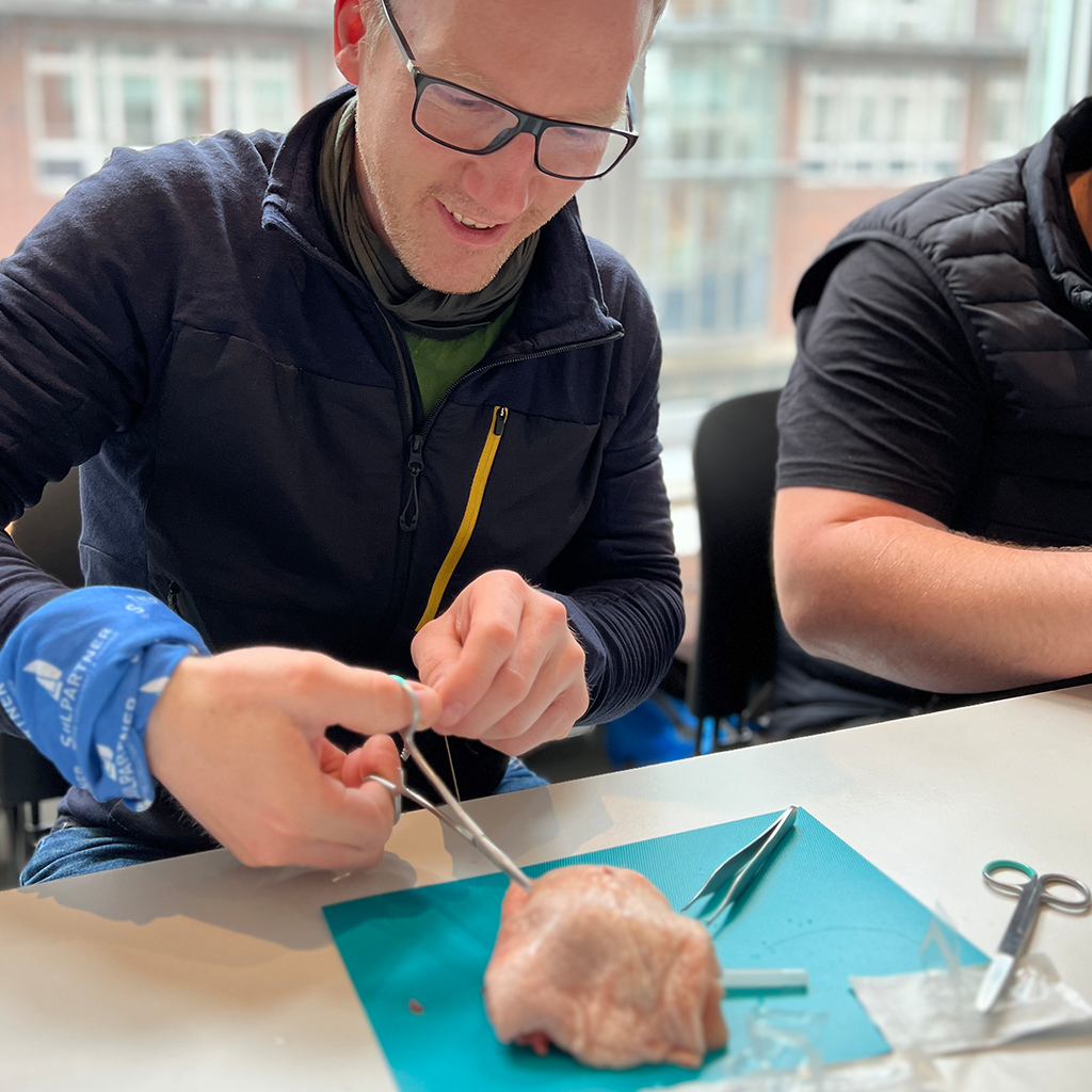 Teilnehmer übt im Medizintraining das Nähen einer simulierten Wunde mit Operationsbesteck.