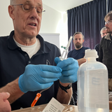 Dr. Jens Kofahl demonstriert im Medizintraining die Vorbereitung von Infusionsbesteck, während Teilnehmer zuschauen.