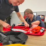 Trainer Michael und Lutz unterstützen Teilnehmer beim Zusammenlegen von Rettungswesten im Offshore-Sicherheitstraining